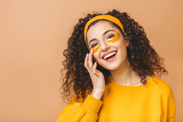 Image of young pure beautiful curly woman isolated over beige background take care of her skin with under eye patches. Image of young pure beautiful curly woman isolated over beige background take care of her skin with under eye patches. one eyed stock pictures, royalty-free photos & images