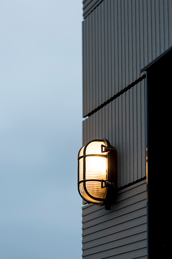 Illuminated outside light on side of house at dusk in metal frame on textured wall