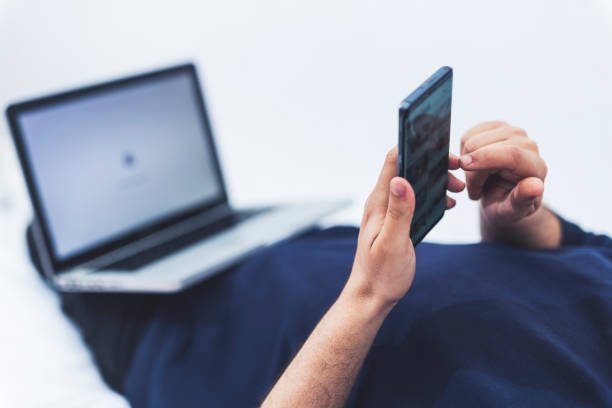 istock close up view of a man using his mobile phone and a lap top while lying on bed 1215141848