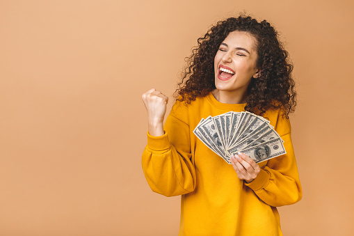 Retrato de una joven alegre sosteniendo billetes de dinero y celebrando aisladosobre sobre fondo beige. photo