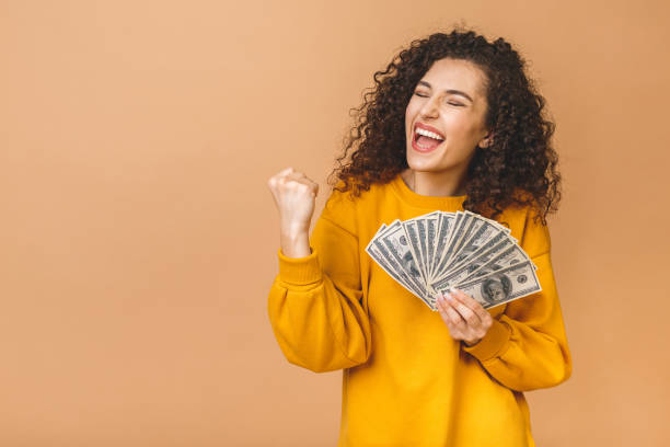 Portrait of a cheerful young woman holding money banknotes and celebrating isolated over beige background. Portrait of a cheerful young woman holding money banknotes and celebrating isolated over beige background. currency paper currency capital wealth stock pictures, royalty-free photos & images