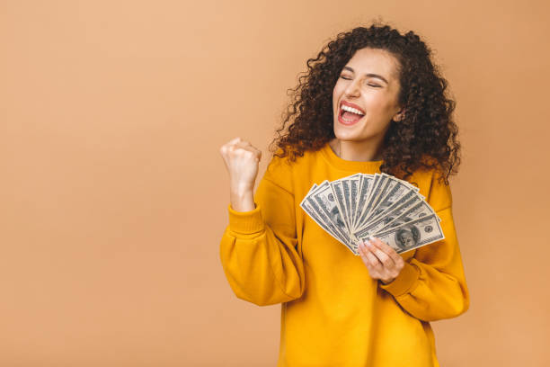 retrato de uma jovem alegre segurando cédulas de dinheiro e celebrando isolada sobre o fundo bege. - holding money - fotografias e filmes do acervo