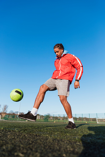 Front view of a young mixed race man kicking the ball on the pitch