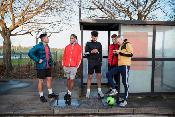 Waiting For The Bus Five young men stand in a line at the bus stop after playing five a side football. bus shelter stock pictures, royalty-free photos & images