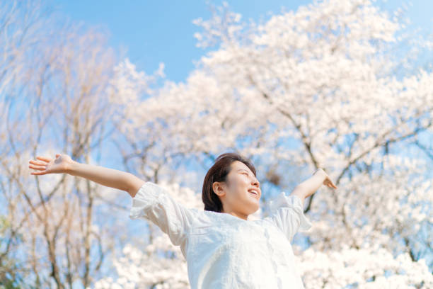 A young woman is stretching her arms in air under a sakura tree.