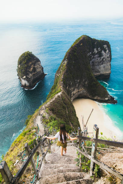 young woman explorer hiking down to the beautiful remote mountain beach in indonesia - nusa lembongan bali island beach imagens e fotografias de stock