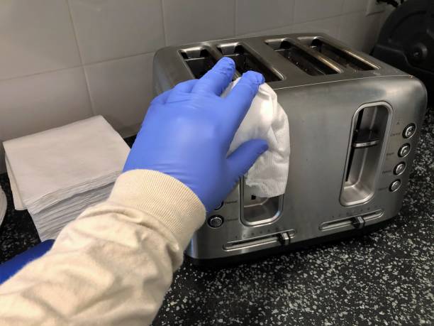 Glove hand with disinfectant wipe cleaning toaster Man disinfecting toaster in kitchen with disinfectant wipe while wearing rubber gloves. Safety precautions to mitigate spread of coronavirus. cleaning stove domestic kitchen human hand stock pictures, royalty-free photos & images