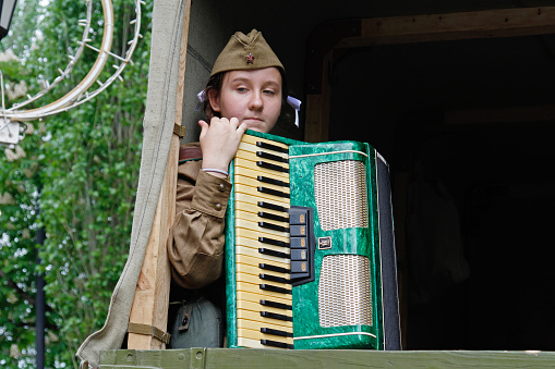 Volgograd, Russia - May 09, 2019: Soviet female soldier in uniform of World War II with an accordion sitting in a military truck on Victory Day in Volgograd