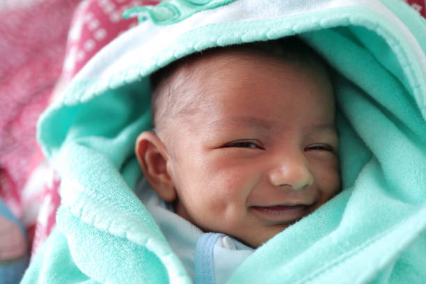 un bebé recién nacido sonriente con hoyuelo en la mejilla envuelto en toalla de color verde marino con capucha con los ojos cerrados con enfoque selectivo en el ojo delantero. - love innocence equipment household equipment fotografías e imágenes de stock