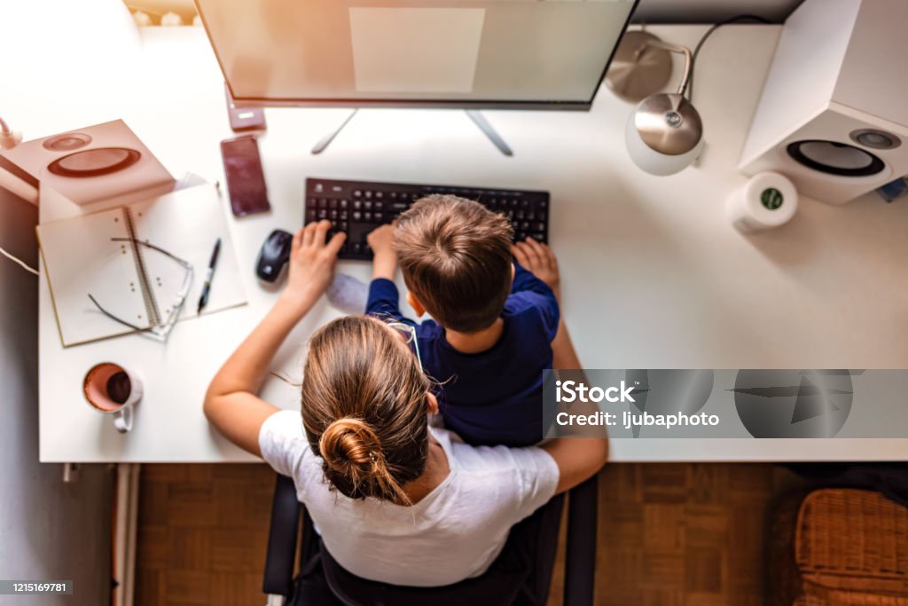 Young mother working from home Overhead view of young mother working on computer with her son sitting in her lap during the day. Child Stock Photo