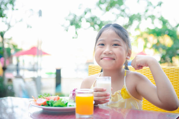 petite fille asiatique mignonne d’enfant faisant la main forte tout en buvant le lait frais - beautiful smiling vegetable calcium photos et images de collection