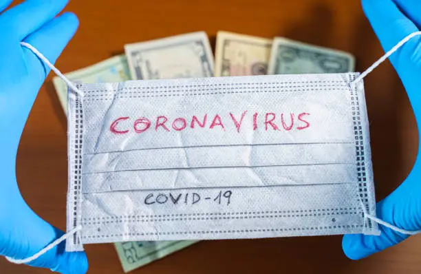 Hand with a face mask with the word coronavirus covering dollar bills . USA stock markets, financial crisis and Stimulus bill caused by the coronavirus outbreak