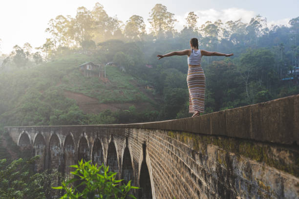 Young woman walking on balance on the Famous Nine Arch Bridge in Demodara, Sri Lanka during sunrise reckless woman walking on the edge of the nine-arches bridge in Sri Lanka ella sri lanka stock pictures, royalty-free photos & images