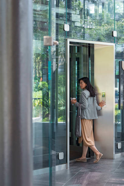 Arriving at Work: Asian Businesswoman Enters an Elevator in an Office Building Asian businesswoman entering an elevator in an office building. outdoor elevator stock pictures, royalty-free photos & images