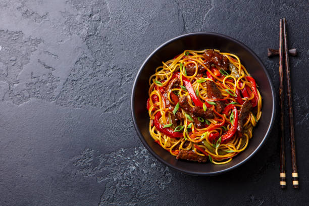 revuelva los fideos con verduras y carne de res en un tazón negro. fondo de pizarra. copiar espacio. vista superior. - chopsticks stir fried vegetable beef fotografías e imágenes de stock