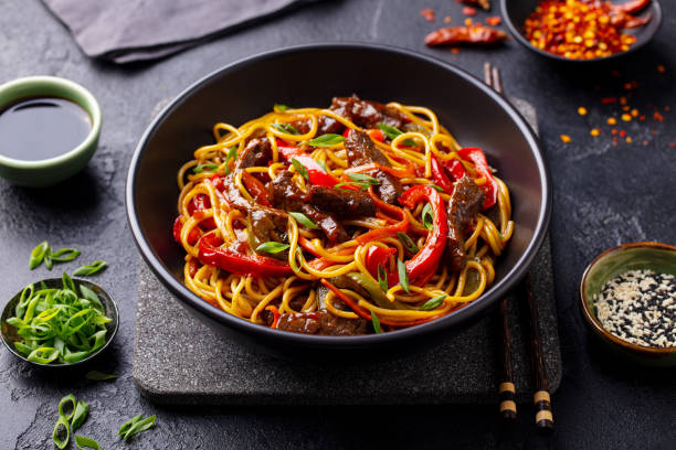 野菜と牛肉を黒いボウルに入れて麺を炒めます。スレートの背景。クローズアップ。 - chopsticks stir fried vegetable beef ストックフォトと画像