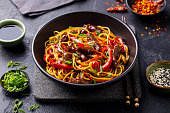 Stir fry noodles with vegetables and beef in black bowl. Slate background. Close up.
