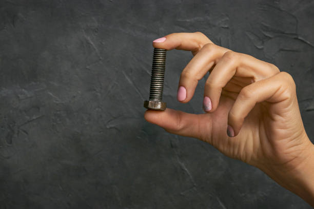 A female hand with a beautiful manicure holds a fresh rusty bolt on a dark background with an original texture.