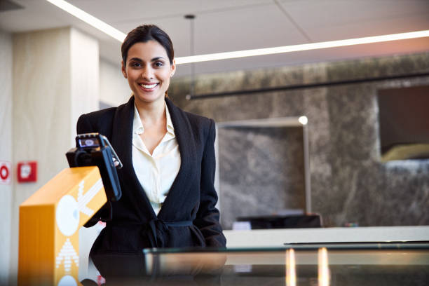 Beautiful lady making contactless payment at airport Smiling young woman holding cellphone while standing by payment terminal stock photo contactless airport stock pictures, royalty-free photos & images