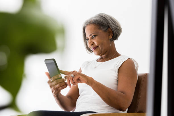 Woman participates in video call with family Attractive senior African American woman smiles while video chatting with her grandchildren. contented emotion photos stock pictures, royalty-free photos & images