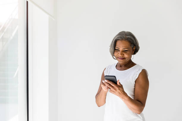 attraente donna anziana attiva che utilizza la tecnologia - senior adult independence lifestyles home interior foto e immagini stock