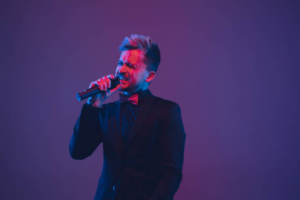 istock Young caucasian musician, performer singing, dancing in neon light on gradient background 1215190077