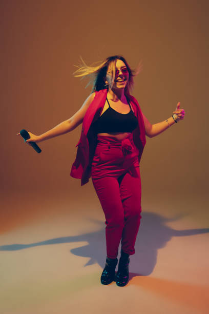 istock Young caucasian female musician, performer singing, dancing in neon light on gradient background 1215190119