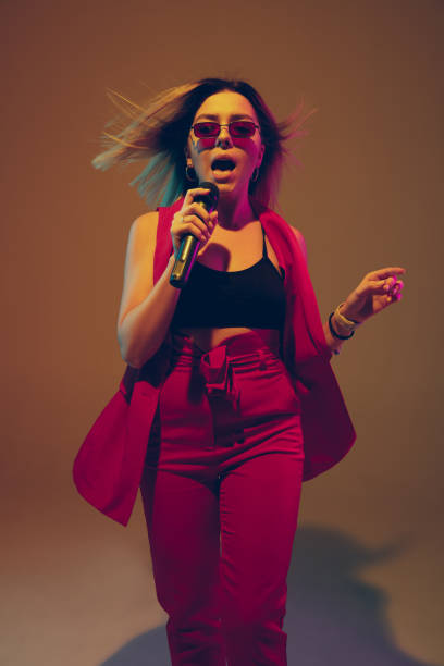istock Young caucasian female musician, performer singing, dancing in neon light on gradient background 1215190122