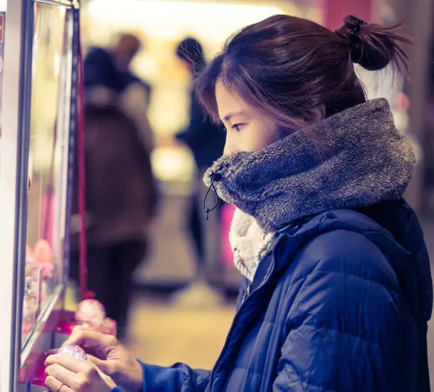 Photo of Japanese girl gamer in winter fashion is playing with crane doll machine in Game center for luck.