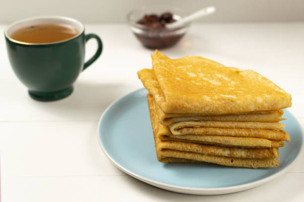 istock Pancakes (Russian Blini) with strawberry jam and tea on a white background. Breakfast. Close up. 1215195444