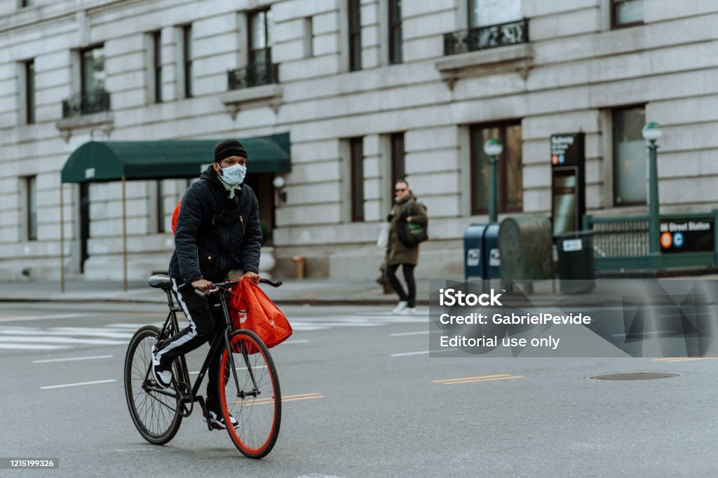 People riding a bicycle in Central Park wearing masks. United States, New York City, Manhattan - March 26, 2020: People riding a bicycle in Central Park wearing masks. Antiviral Drug Stock Photo
