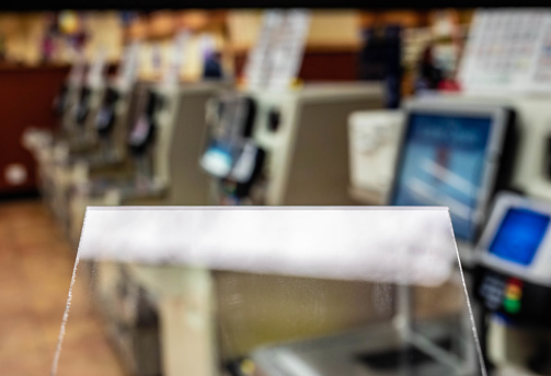 Generic close up of a sneeze guard partition pane in a supermarket checkout area protecting shoppers and products from germs.