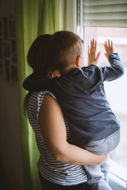 istock Mom and son looking through window at home 1215200395