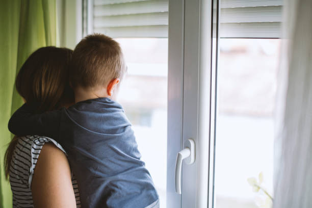 Mom and son looking through window at home stock photo