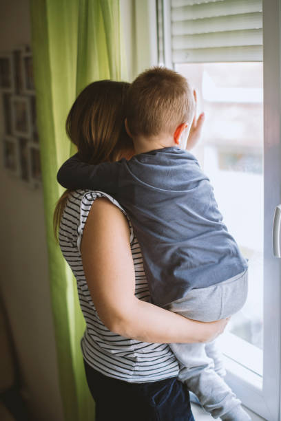 istock Mom and son looking through window at home 1215201772