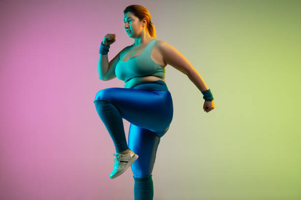 istock Young caucasian plus size female model's training on gradient purple green background 1215203326