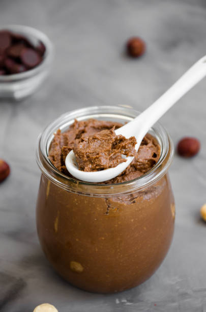 istock Homemade crispy chocolate hazelnut paste in a glass jar on a dark background. Vertical orientation. Close up 1215206111