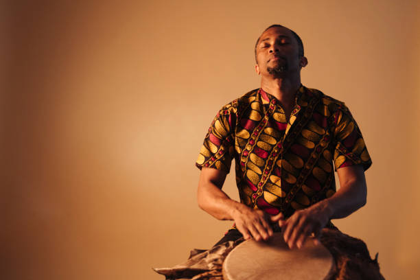 african american man muzyk gra tradycyjne bębny w brązowym tle przestrzeni kopii. - drum beats zdjęcia i obrazy z banku zdjęć