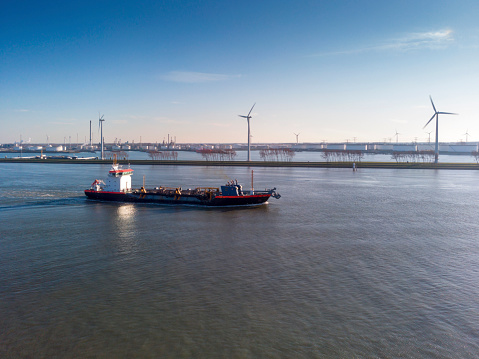 Aerial view on a ship over the Meuse river with the Europoort industrial area in the background. The photo was taken during the outbreak of COVID-19 in the Netherlands. During the outbreak, much of social life came to a halt and people should stay at home as much as possible. Crucial industries, including food production and transportation, are allowed to continue operating.