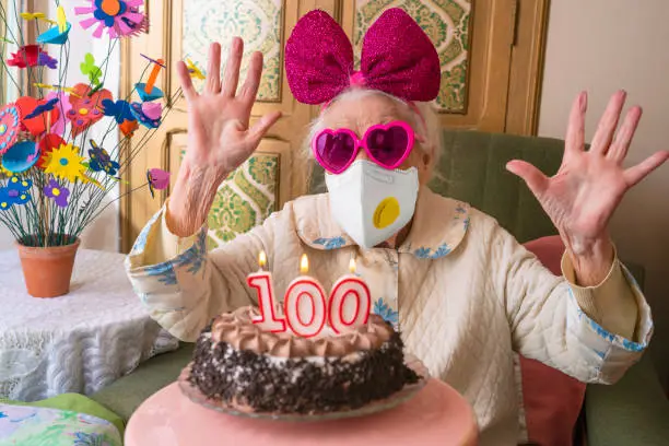 Photo of Coronavirus COVID-19 pandemic confinement with mask in 100 years old birthday cake old woman humor