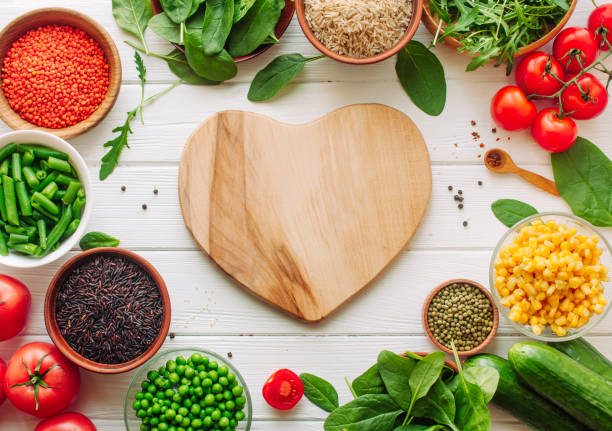 Wooden heart shape board surrounded by fresh vegetables, groats