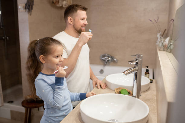 Cute little girl and her happy father with toothbrushes going to brush teeth Cute little girl and her happy young father with toothbrushes going to brush teeth while standing in bathroom in front of mirror brushing teeth stock pictures, royalty-free photos & images