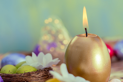 Greeting card Easter burning golden candle and chocolate eggs in colored foil. Festive easter concept. Blurred background and glowing bokeh. Copy space.