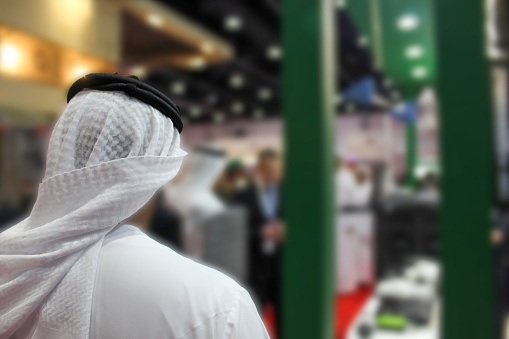 Arab man standing with his back at a exhibition. Blurred background.