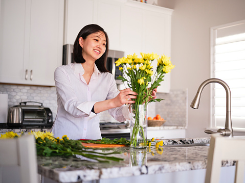 A Japanese woman preparing a flower arrangement in her home kitchen.