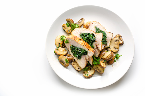 chicken breast fillet stuffed with spinach, served with mushrooms and parsley garnish on a plate, isolated with shadows on a white background, copy space, high angle top view from above