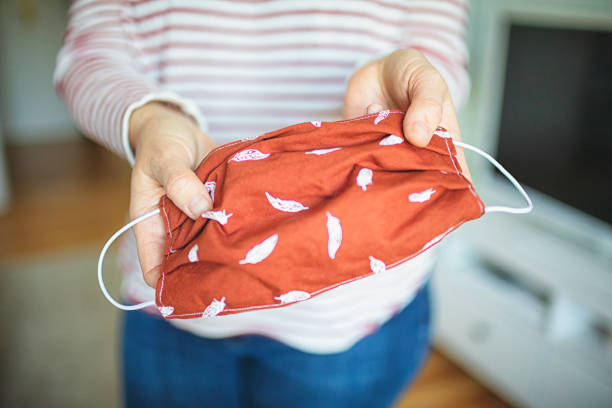 젊은 여성은 바이러스와 박테리아로부터 보호하기 위해 자수 마스크를 보여줍니다 - textile sewing women part of 뉴스 사진 이미지