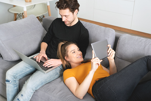 Couple using fast home internet with laptop and digital tablet. Woman and man on sofa in living room