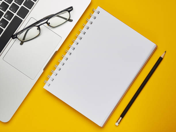 istock Workplace - laptop, notebook, glasses and pencil for remote work on a yellow background table. Freelance desktop for home or office. Background with copy space. 1215229024
