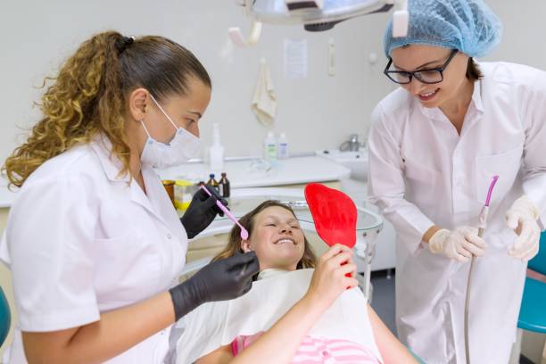 Teenager girl in dental chair with mirror looking at her teeth Teenager girl in dental chair with mirror looking at her teeth, smiling doctor and assistant. Medicine, dentistry and healthcare concept Dental Hygienist Schools stock pictures, royalty-free photos & images